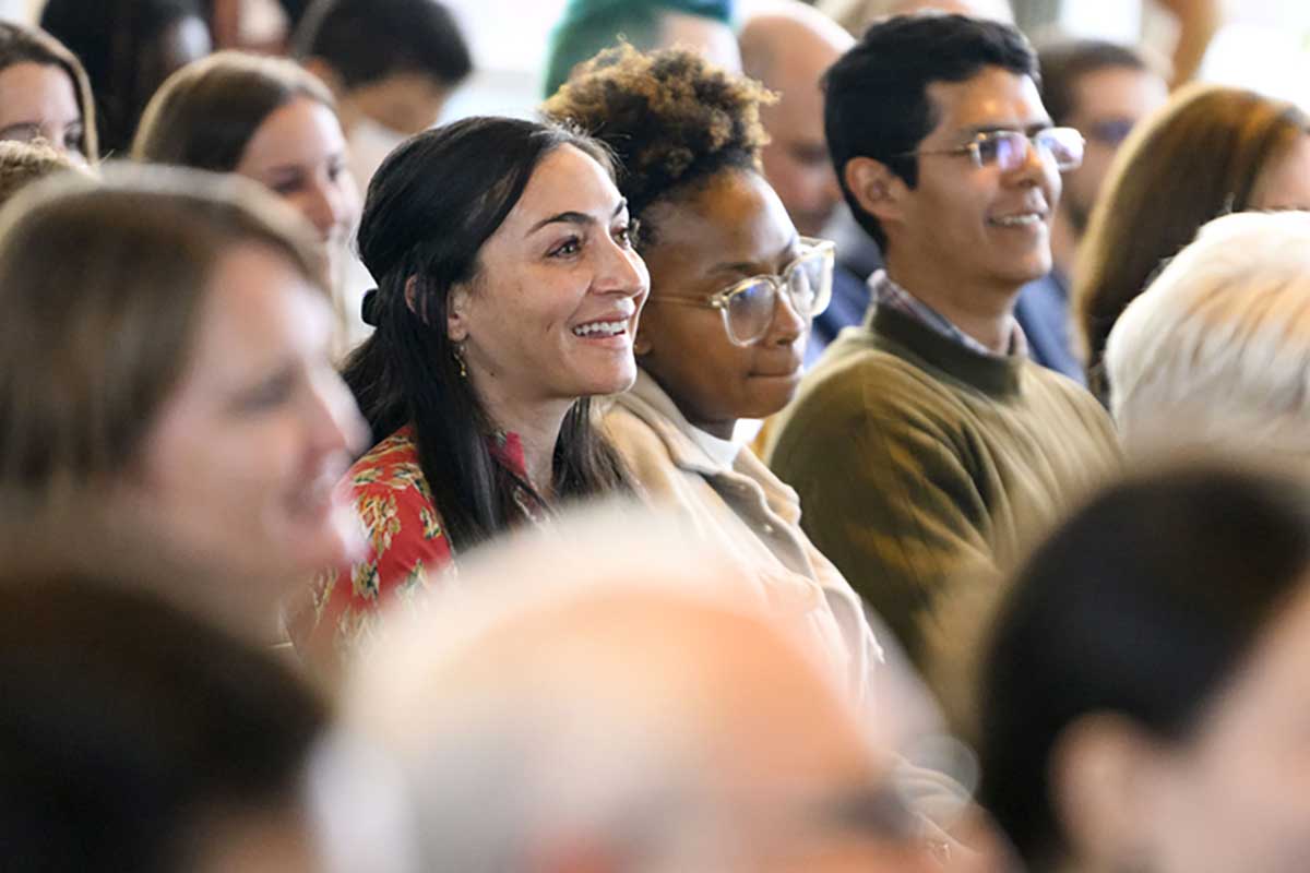 Several rows of Khoury staff and faculty sit in an auditorium and watch a panel discussion