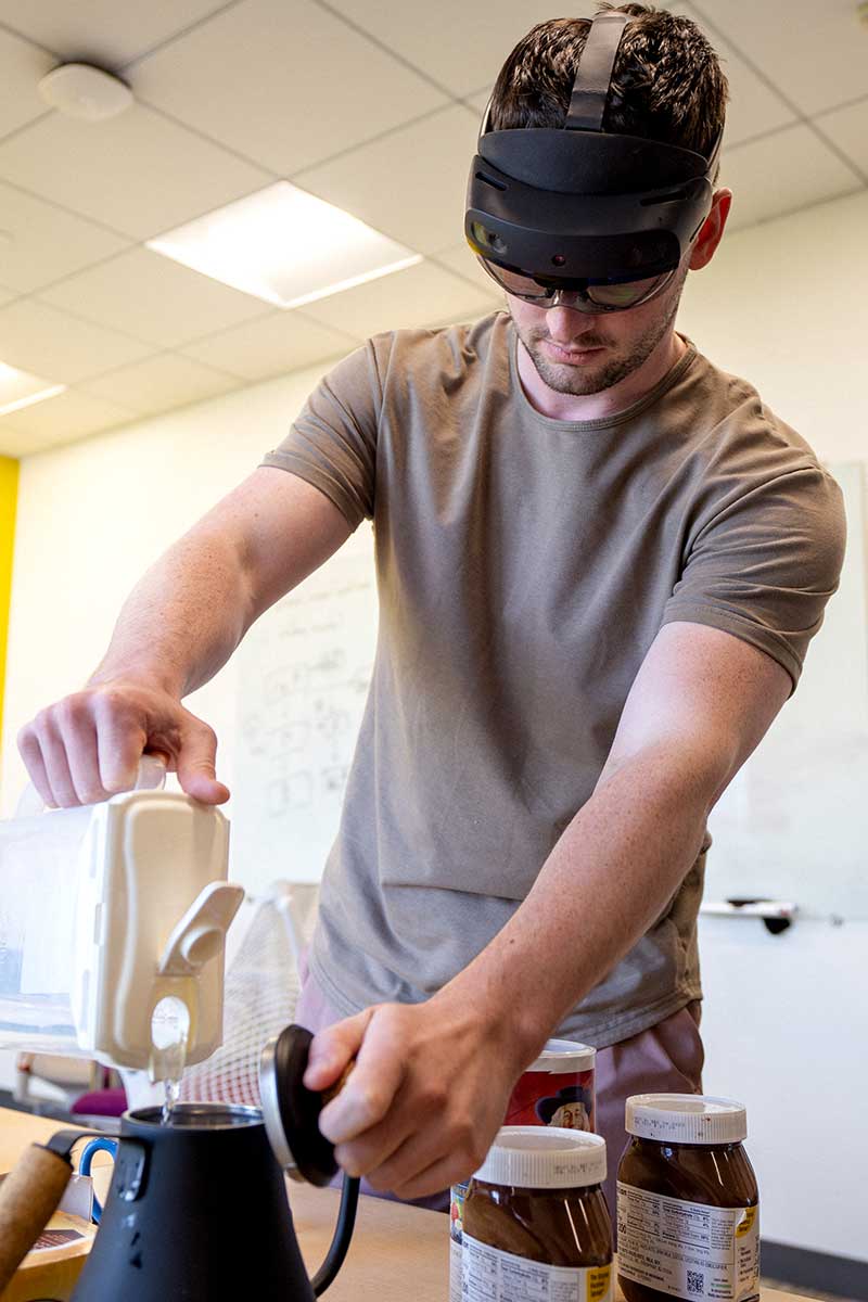 A student wears a virtual reality headset while pouring water into a pitcher