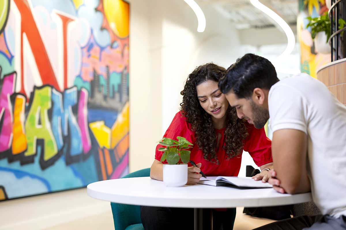 Two students sit at a table and look at an open notebook at Northeastern Miami