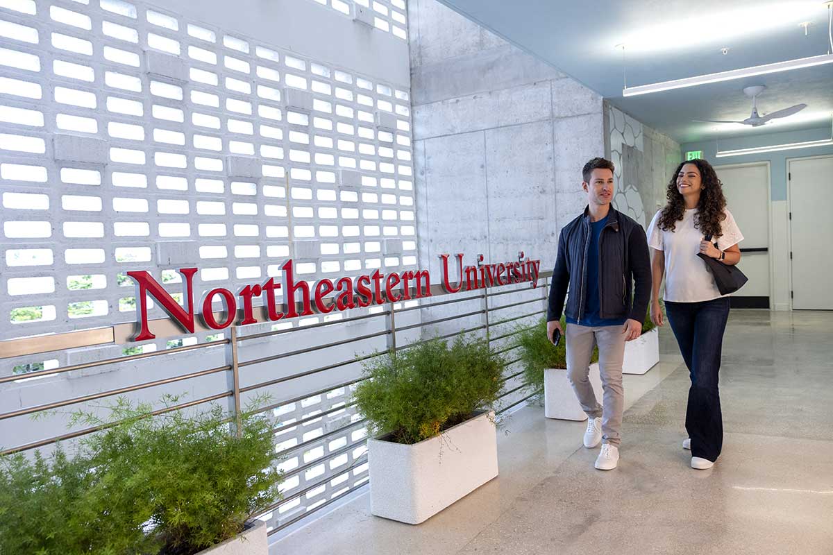 Two students walk by a Northeastern University sign at the university's Miami location