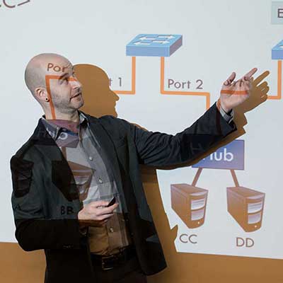 Christo Wilson gestures at a large presentation screen during a class