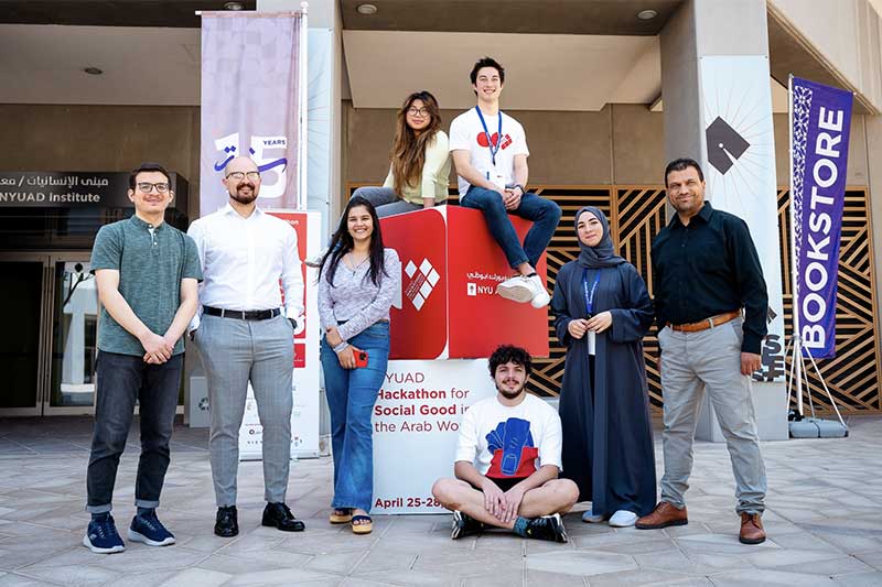 Shannen Espinosa and another student sit on top of two large stacked cubes set up outside the building of the International Hackathon for Social Good in Abu Dhabi