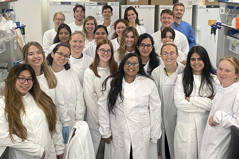 Shannen Espinosa (lower left corner) poses for a photo with 21 other colleagues in a lab at Oxford