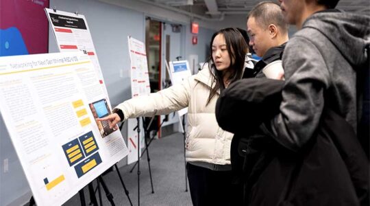 A Khoury graduate student points at her research poster while explaining her project to two onlookers