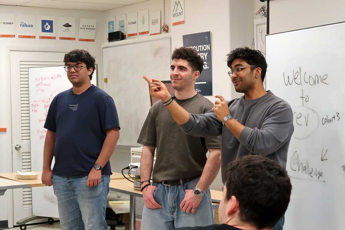 Three members of Rev stand in front of a whiteboard during a club meeting