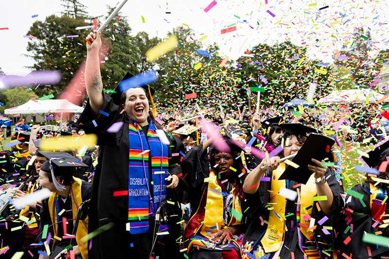 Graduates hold up their diplomas while confetti falls