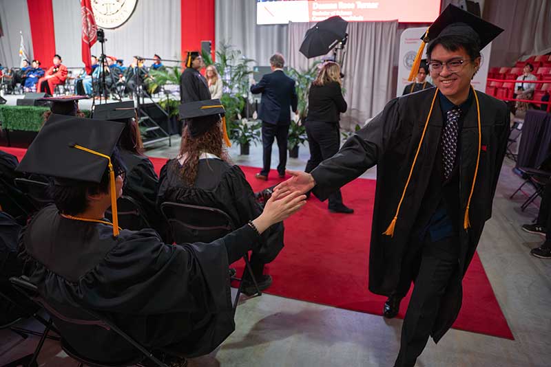 A graduate walking to the stage high fives a seated graduate