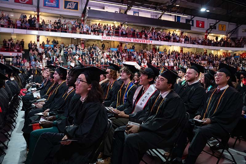 Several rows of seated graduates watch the ceremony