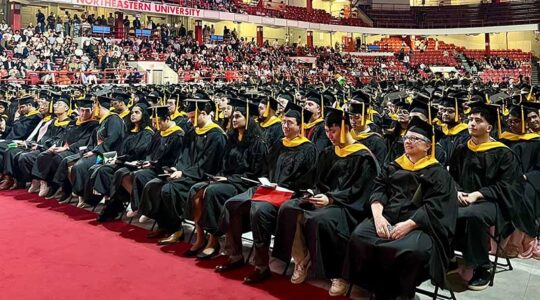 Dozens of rows of graduates in dressed in caps and gowns watch the stage
