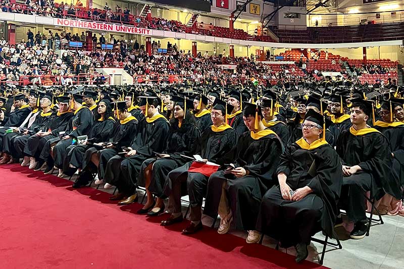 Dozens of rows of graduates in dressed in caps and gowns watch the stage
