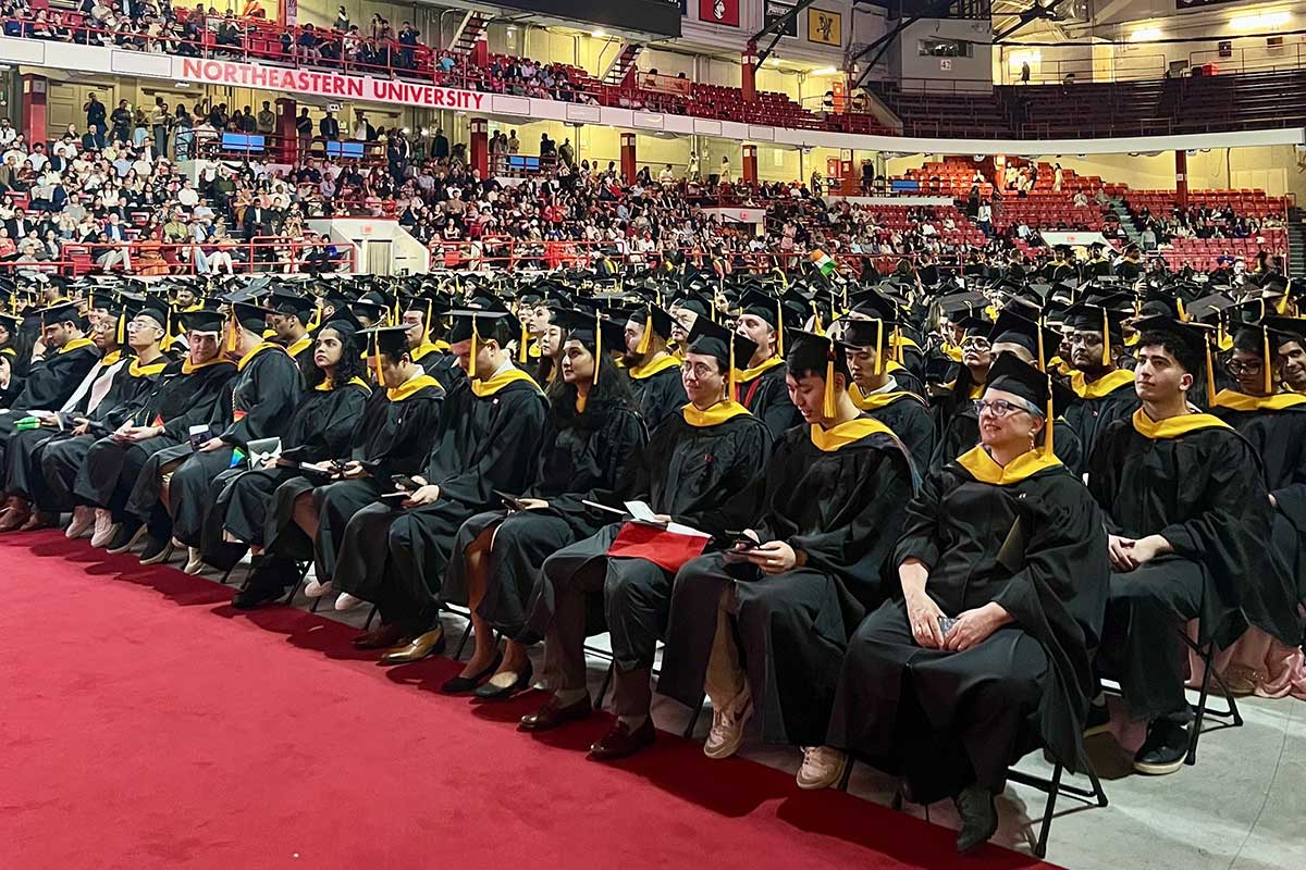 Dozens of rows of graduates in dressed in caps and gowns watch the stage