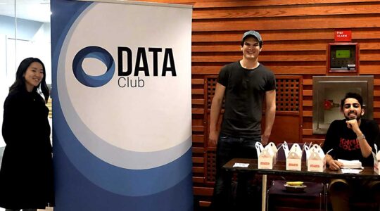 Three students pose for a photo standing around a DATA Club banner
