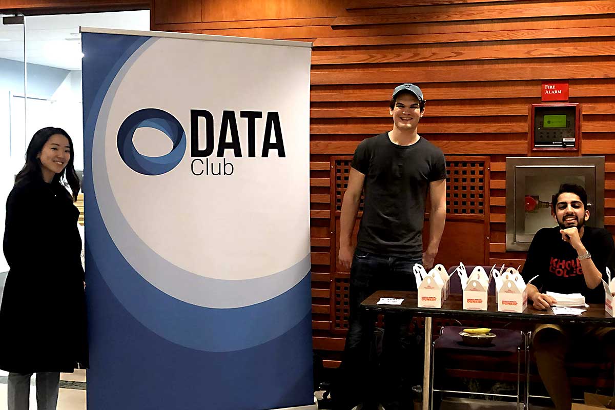 Three students pose for a photo standing around a DATA Club banner