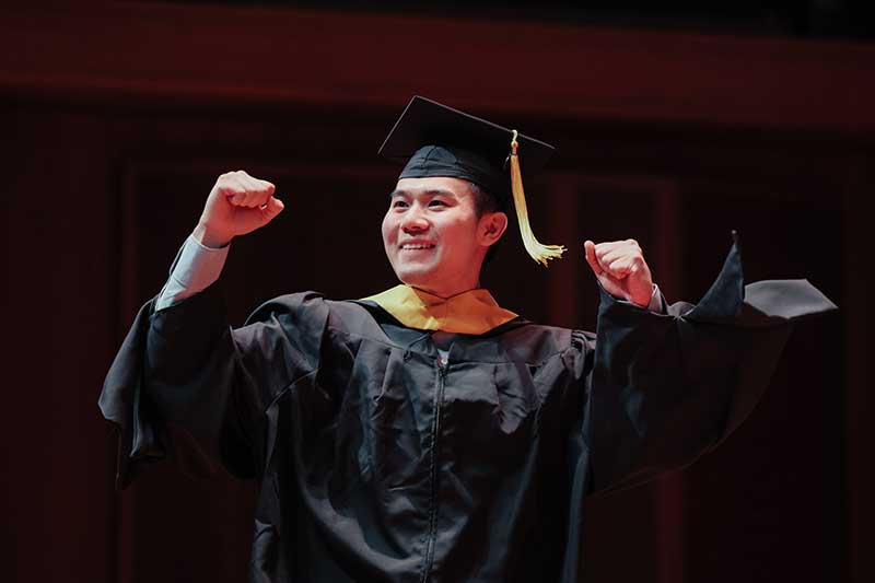 A Khoury graduate raises his hands in triumph before receiving his diploma