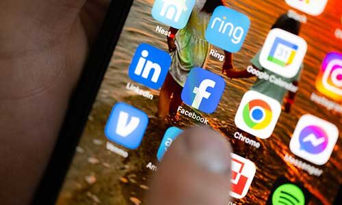 A thumb hovers over the Facebook icon on a phone screen