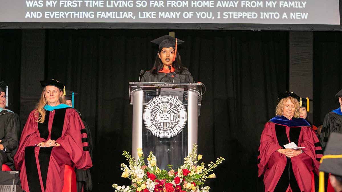 Student speaker Soumya Hukkeri speaks behind a podium with the Northeastern seal