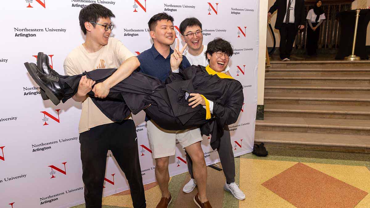 Three attendees hold a Khoury graduate horizontally in their arms