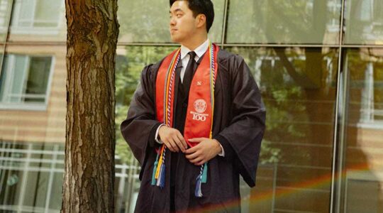 Jeff Pan poses while wearing his graduation robe and a red sash