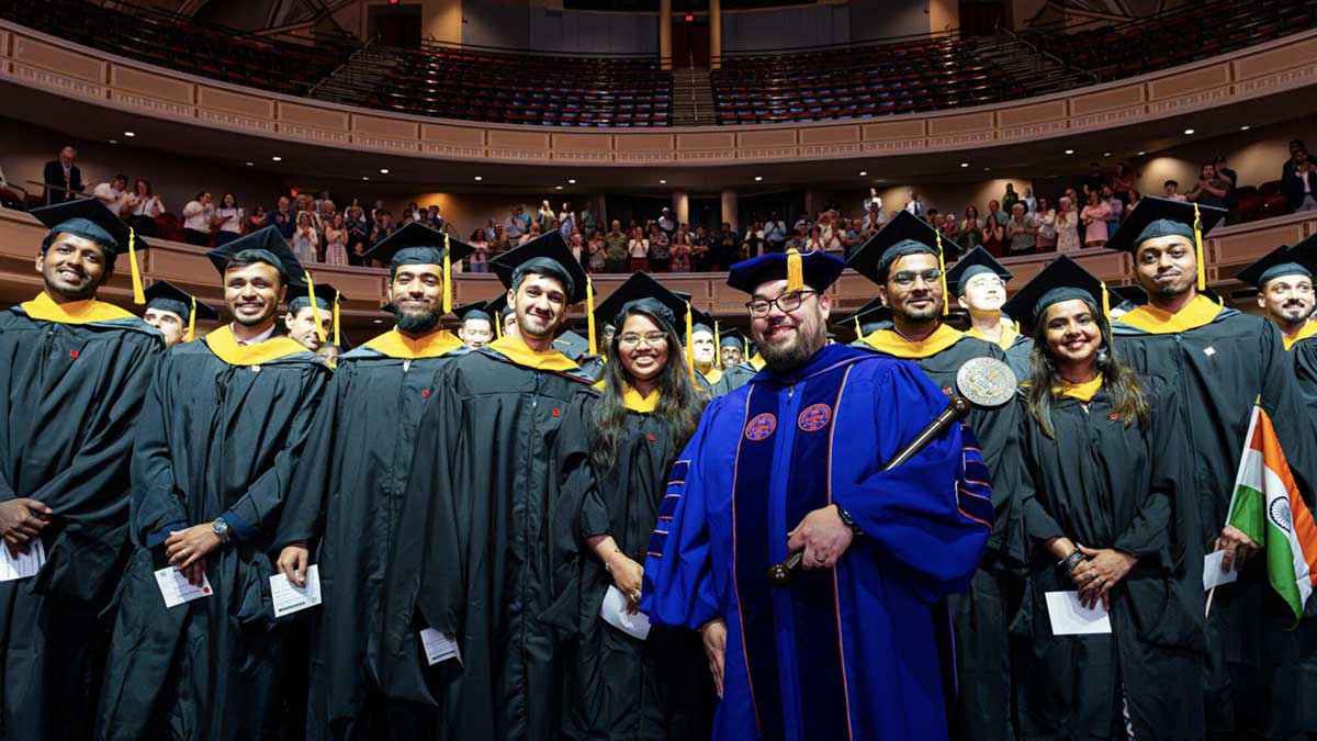 Alan Jamieson, Khoury College’s East Coast associate dean of computing programs poses with graduates in their regalia.