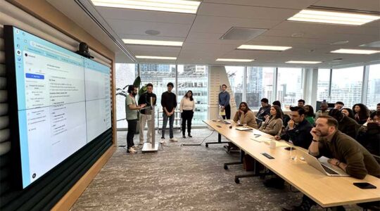 One of the hackathon teams presents a project on a large screen at the front of a conference room