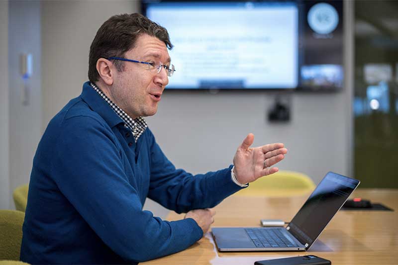 Engin Kirda speaks to students while sitting at a large table with his laptop in front of him