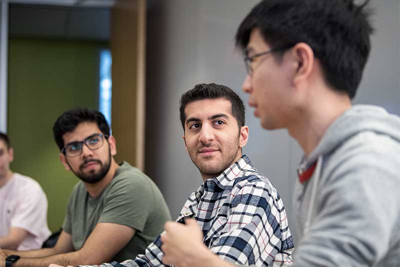 Seyed Ali Akhavani sits at a table while listening to another student talk about their project