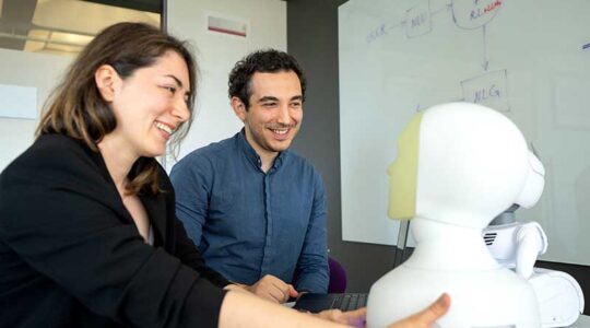 Khoury faculty Malihe Alikhani (left) grasps a device resembling a human face as a student looks on
