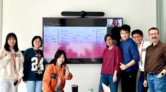 5 students and 2 faculty members pose for a photo standing beside a large screen showing their Career Pathway app