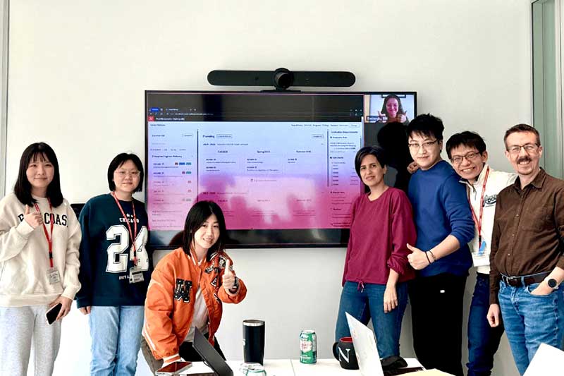 5 students and 2 faculty members pose for a photo standing beside a large screen showing their Career Pathway app