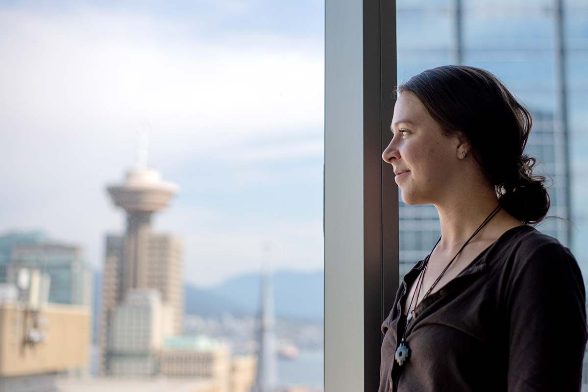 A student in Vancouver looks out a window that looks out on the Vancouver skyline with the Harbour Centre skyscraper in the background