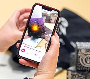 A photo showing a hand grasping a mobile phoe that is showing a video of the formation of the solar system