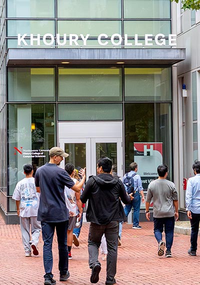 Groups of students walk to the doors of West Village H. A Khoury College sign is visible above the door.