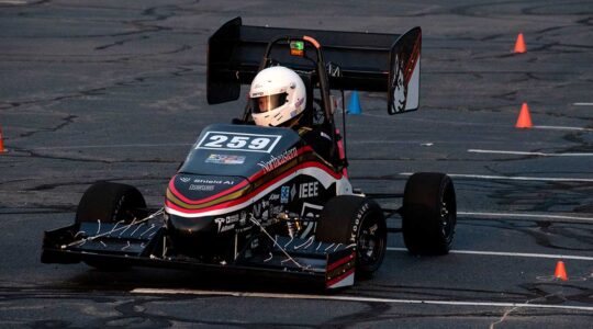A Northeastern Electric Racing club member drives the club's vehicle around cones in a parking lot