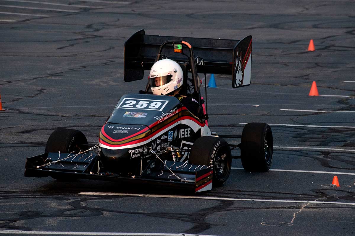 A Northeastern Electric Racing club member drives the club's vehicle around cones in a parking lot