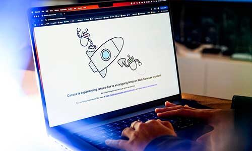 A person types on a laptop showing a screen that says the Canvas app is experiencing issues due to an Amazon Web Services incident