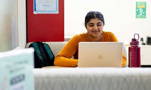 A woman sits at a table working on a laptop