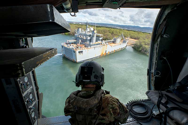 A rescuer looks out a helicopter door at a disabled ship close to land