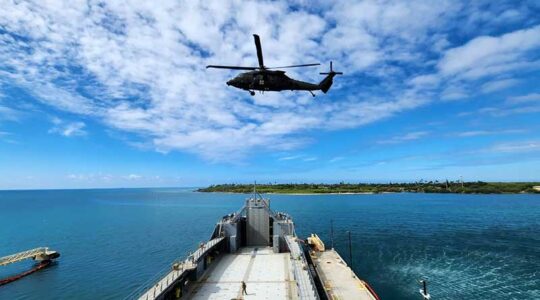 A helicopter flies over a pier jutting out into a body of water