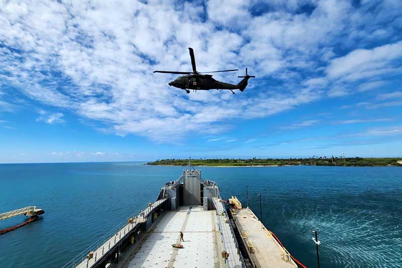 A helicopter flies over a pier jutting out into a body of water