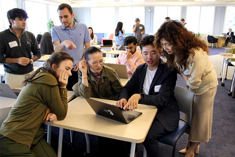 Several Khoury Silicon Valley students huddle around a laptop while Ilmi Yoon looks at their work