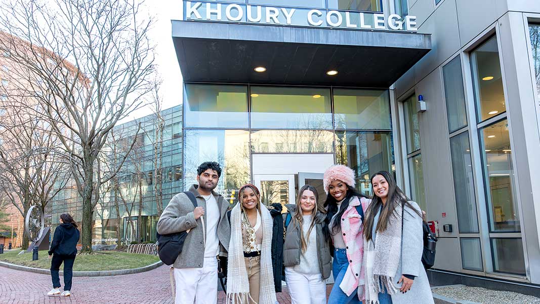 Five Khoury students pose for a photo standing in front of the Khoury College sign above the main entrance of West Village H