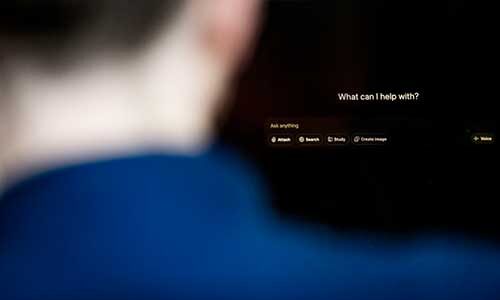 A person looks at a computer screen with a prompt that says, "What can I help with?"