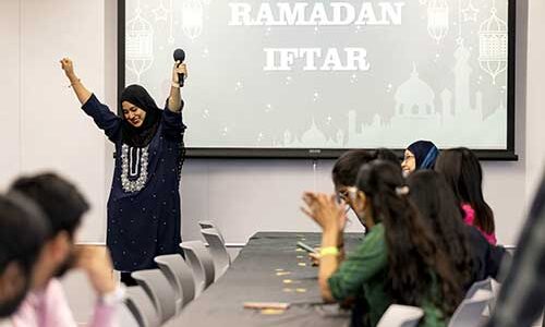 A student raises her hands in celebration after giving a presentation while other applaud