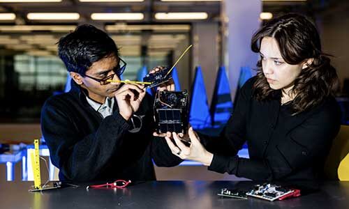 Northeastern Satellite Lab president Ganesh Danke, left, and chief mechanical engineer Laura Tomarossi Teixeira showcase satellite components in in the EXP building on the Boston campus.