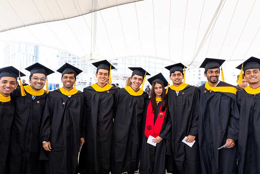 Nine Khoury graduate students wearing caps and gowns pose for a photo
