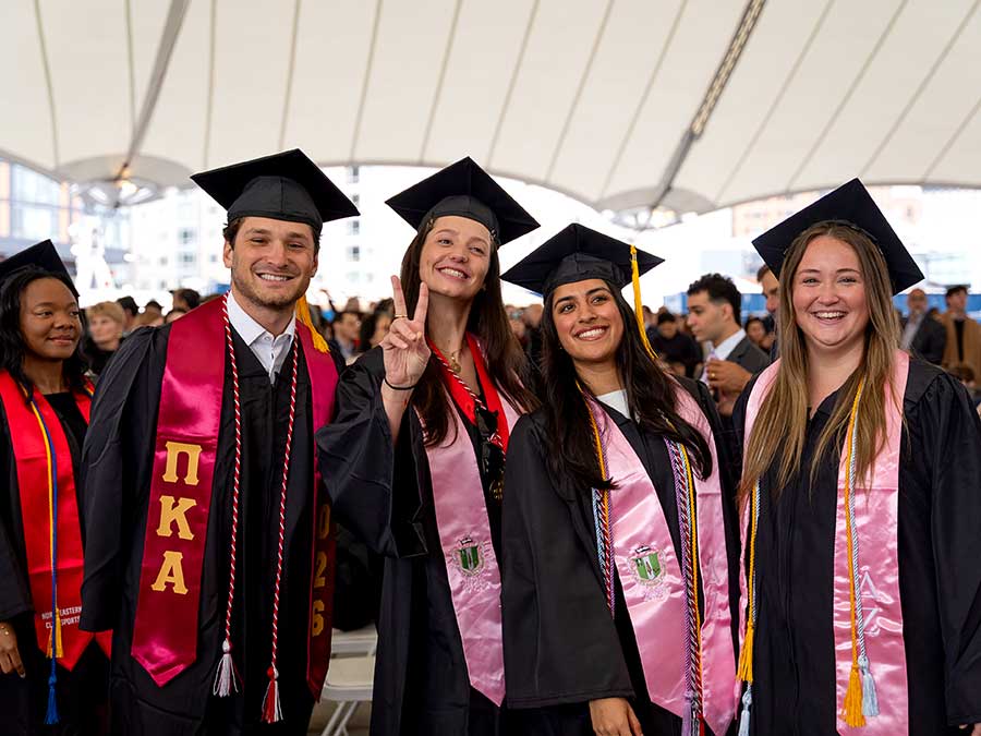 Four Khoury graduates wearing caps, gowns, and sashes pose for a photo