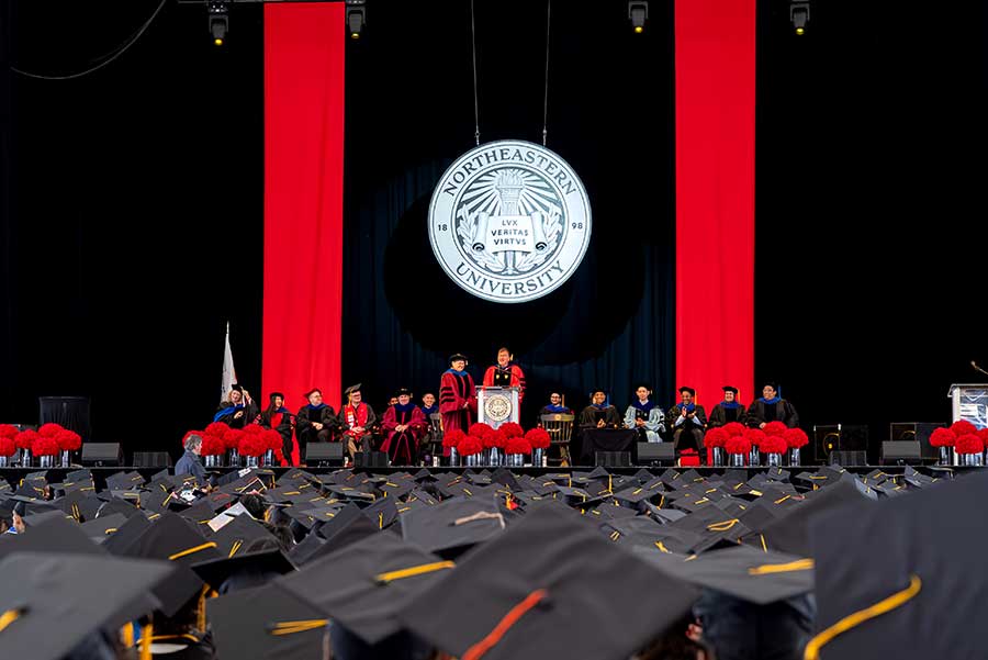 A view of the Khoury commencement stage with rows of seated graduates in the foreground