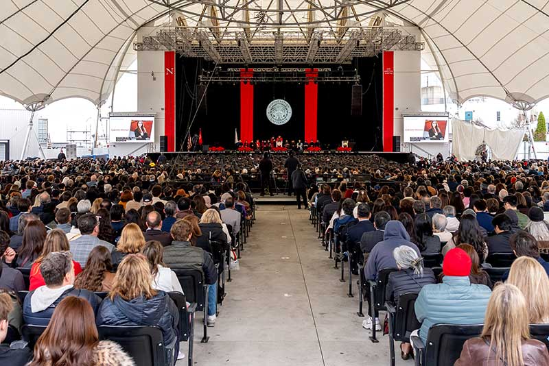 A wide view taken from behind the large commencement audience viewing the stage