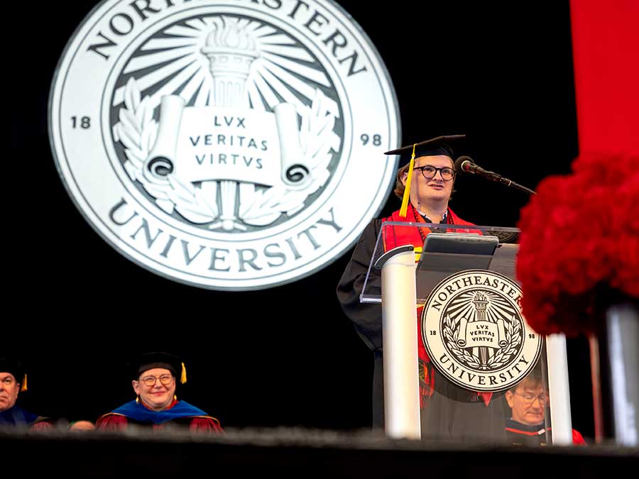 Khoury undergraduate speaker Misha Ankudovych gives his speech behind a podium with the Northeastern University seal hanging in the background