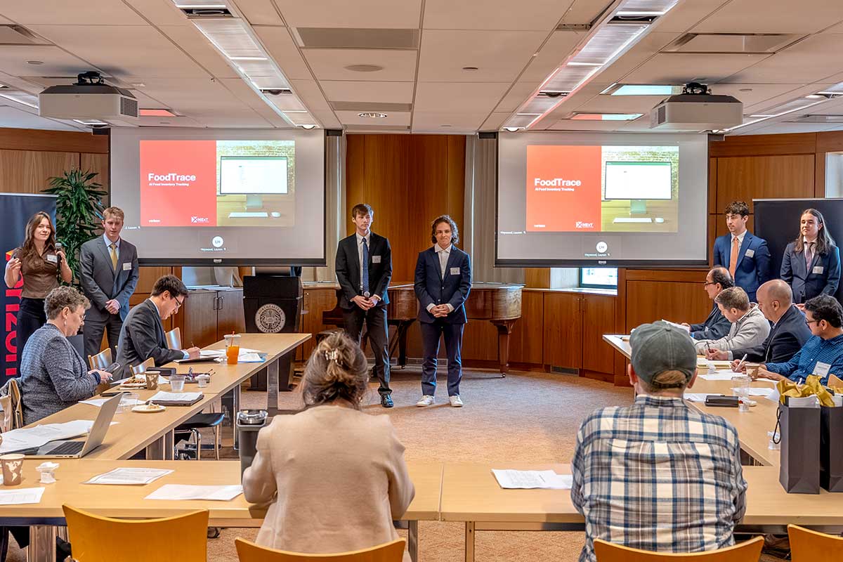 A team of six students present a project titled "FoodTrace" in a large conference room to an audience sitting at a u-shaped table